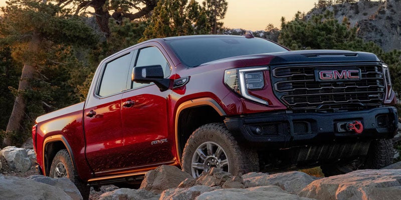 Red GMC Sierra 1500 off-roading on rocky terrain in a forest setting